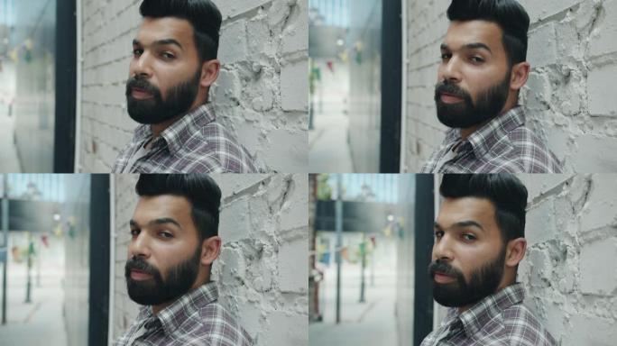 具有超凡魅力的阿拉伯男子看着站在砖墙背景上的相机的慢动作特写肖像
