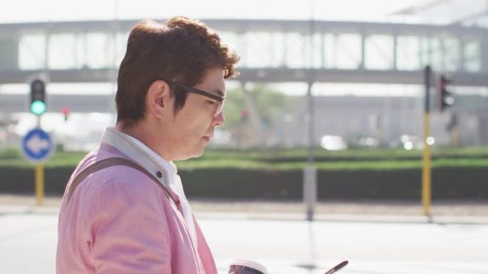 亚洲男子在街上散步时喝咖啡和使用智能手机