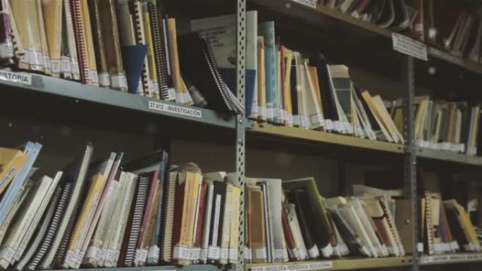 许多书籍，教科书，活页夹和螺旋笔记本放在学校图书馆的存储金属架子上。特写。