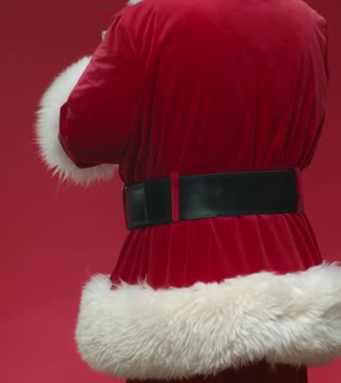 一个在红色背景上转身微笑的圣诞老人，拿着一个小礼品盒，在视频结尾的镜头前展示