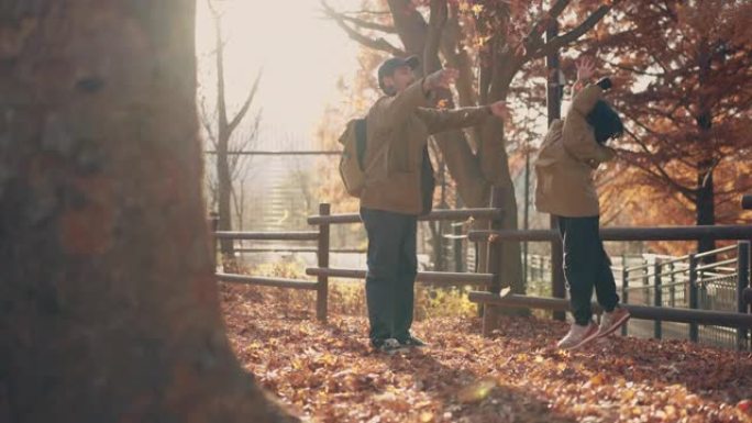 亚洲父亲和可爱的男孩在秋天在公园扔秋叶。