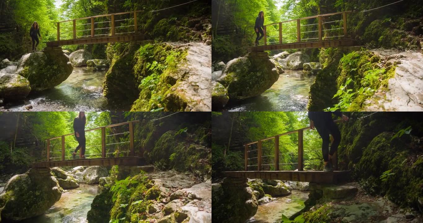 年轻女子在绿色景观的山间小溪上的木桥上行走