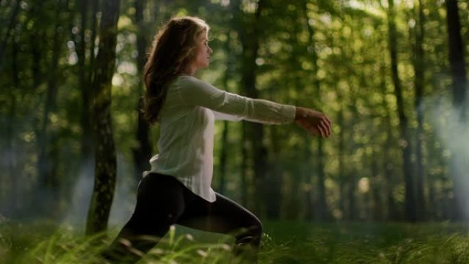 SLO MO年轻女子在朦胧的绿色森林中练习瑜伽