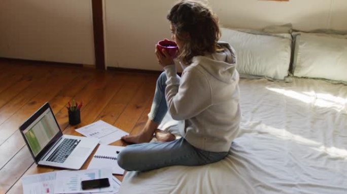 混血妇女在家工作，坐在床上用笔记本电脑，在小屋喝茶