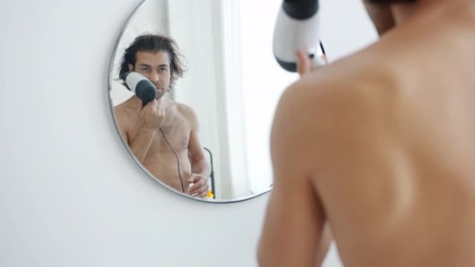 英俊的年轻人在浴室里用电动吹风机照镜子吹干头发的慢动作