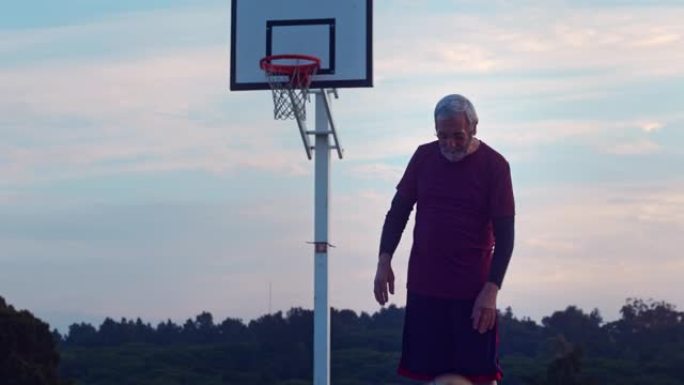 高级男子在日出时在户外球场上弹跳篮球