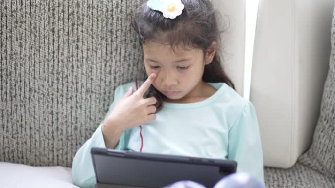 小女孩在线学习沙发上的数字平板电脑在家里的客厅