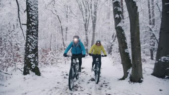 在下雪的冬季小径上与前灯骑行ebikes的情侣