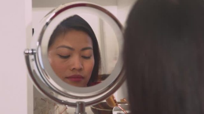 特写: 美丽的菲律宾女人在镜子反射中涂抹黑色睫毛膏