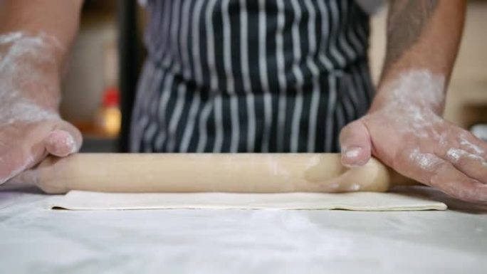 面包店的特写手在面团上使用木制Rolling面杖做饭。专业厨房的厨师用面粉准备食物，制作意大利面食。