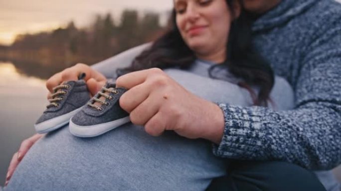 男子在怀孕妻子的肚子上玩婴儿鞋