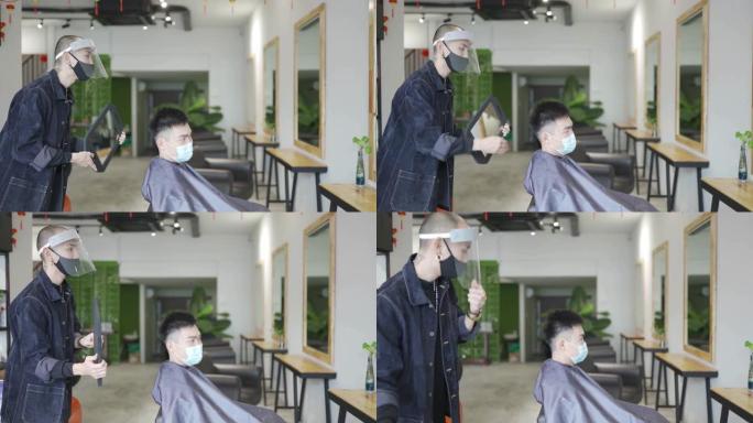 亚洲华人发型师与保护工作服拿镜显示他的客户后他的头发在美发沙龙剪完他的头发