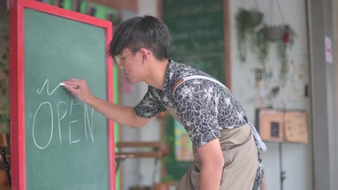 亚洲中国年轻咖啡馆咖啡师服务员自助餐厅工作人员在咖啡馆餐厅外面准备营业的黑板上用粉笔写 “开放” 字