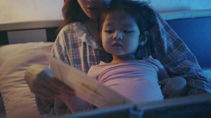 亚洲母女在卧室里看书，指着家里的书。睡前故事