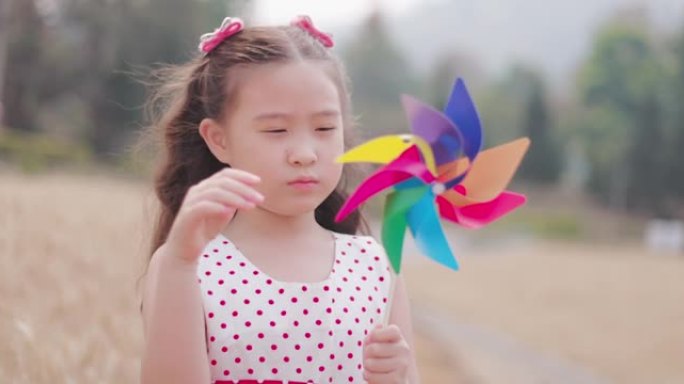 快乐的亚洲小女孩拿着折纸风车在大麦田里奔跑