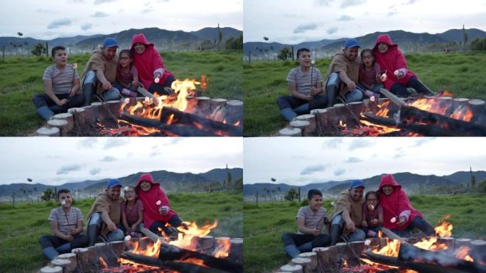 美丽的农民家庭在田间工作后享受篝火，烤棉花糖说话和微笑