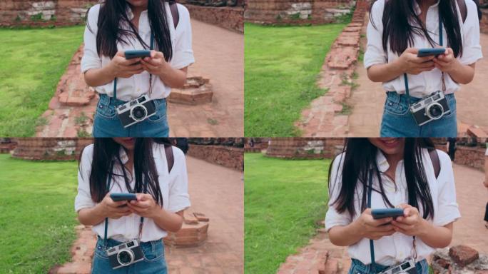 特写年轻亚洲背包客博主女子休闲用相机看屏幕在手机上搜索导航应用的位置。