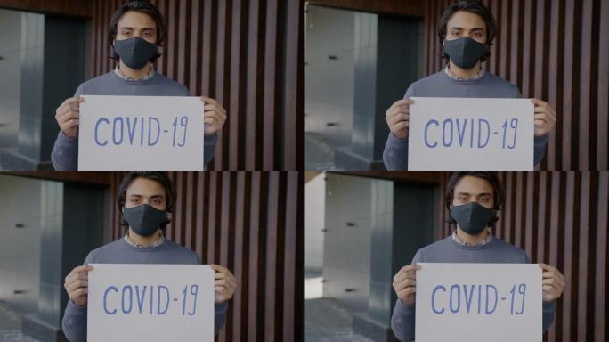 阿拉伯男子手持新型冠状病毒肺炎海报站在户外戴着口罩的慢动作肖像