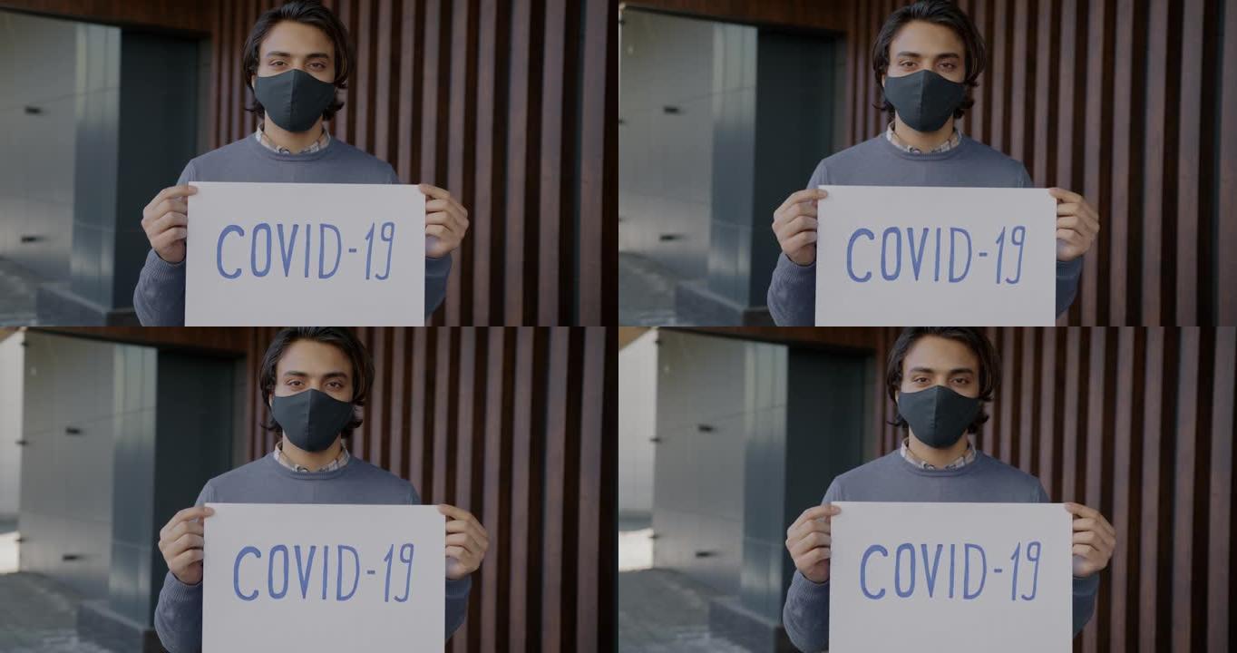 阿拉伯男子手持新型冠状病毒肺炎海报站在户外戴着口罩的慢动作肖像