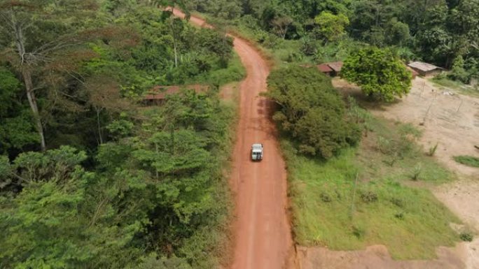 在非洲中部热带雨林的伐木公路上驶过一个小村庄的车辆的鸟瞰图