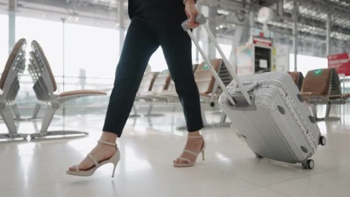 穿着高跟鞋的女人的腿带着带轮行李在机场行走