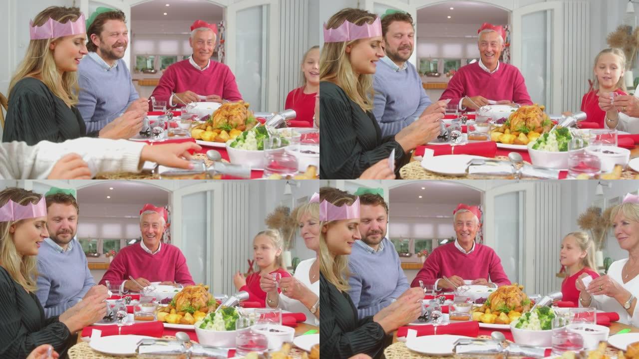 戴纸帽的多代家庭在一起吃饭的同时阅读圣诞饼干笑话