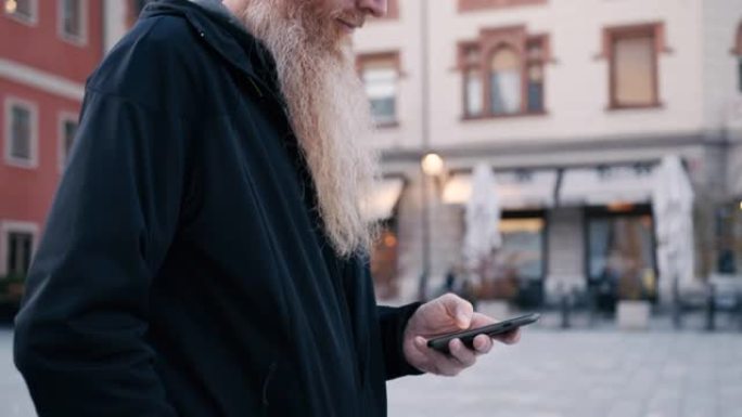 在城市散步时，留着长胡须的男人使用智能手机