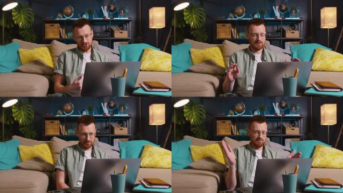快乐的年轻积极的红头发男老师戴着眼镜，在舒适的家里用笔记本电脑网络摄像头视频通话。