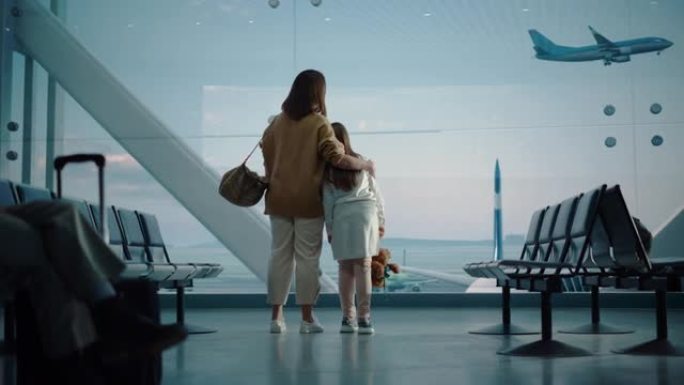 机场航站楼: 美丽的母亲和可爱的小女儿等待他们的假期航班，看着窗外的飞机进出。航空枢纽登机休息室的年