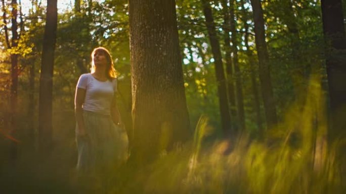 穿着白色长裙的SLO MO女人在日落时在森林中行走