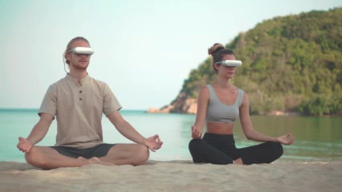 25-29岁的拉丁美洲和西班牙裔年轻夫妇戴着技术虚拟现实耳机，早上在夏日海滩上的户外练习瑜伽。Met