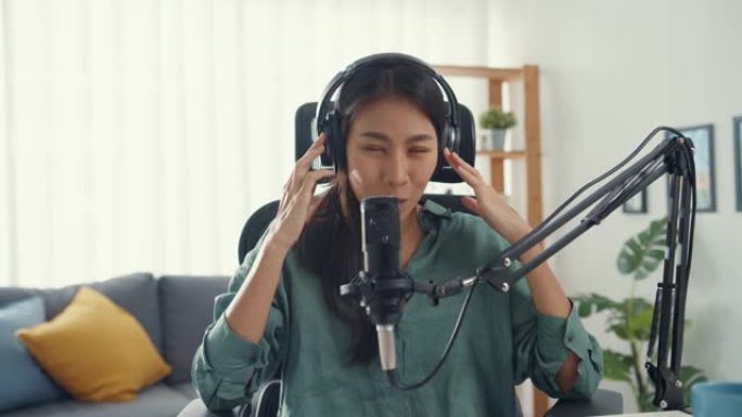快乐亚洲女孩用耳机和麦克风录制播客看相机谈话，在她的房间里休息一下。