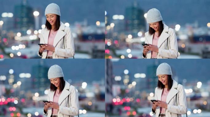 女人在手机上阅读有趣的文字，在城市的寒冷夜晚大笑。时髦开朗的女性发送消息或使用移动应用程序预订出租车