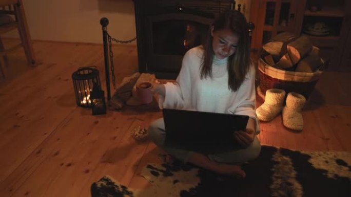女人在家里用笔记本电脑在壁炉旁喝茶