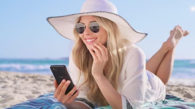 一个快乐的年轻女子使用电话，在海滩上放松。开朗的女性发短信和滚动社交媒体。享受热带度假胜地的暑假假期