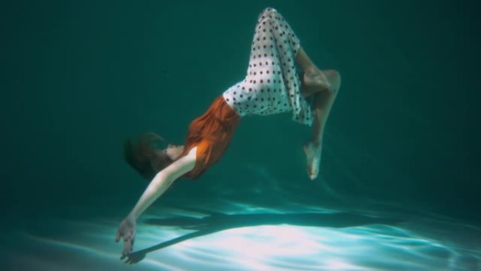 侧视图美丽年轻优雅的舞者女人做后翻舞，在水下穿着波西米亚服装慢动作摆姿势。
