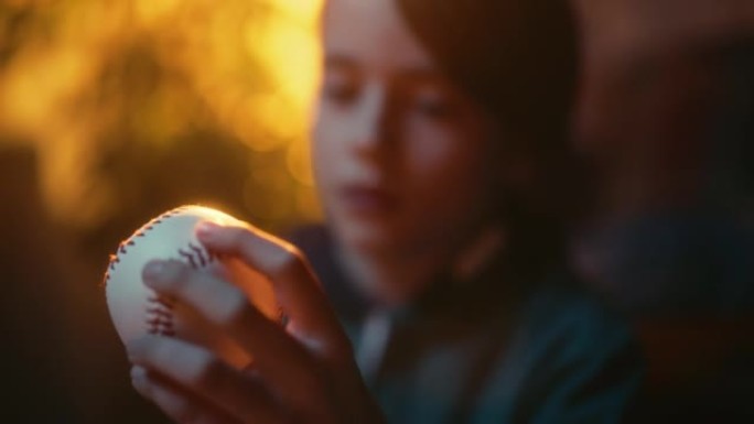 一个年轻的体育迷在家中拿着白色棒球球的特写肖像。兴奋的男孩看着球，把球转了过来。在怀旧复古的童年概念