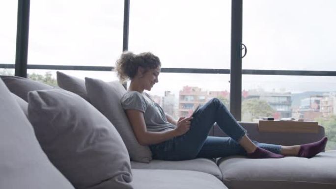 年轻女子在家时，用平板电脑在沙发上观看视频放松