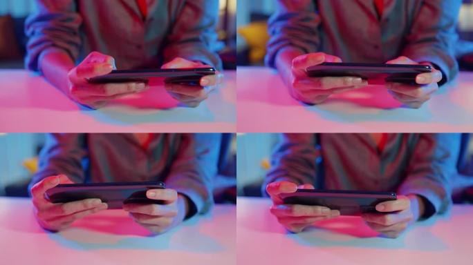 特写镜头亚洲女孩游戏玩家使用智能手机玩网络游戏彩色霓虹灯在客厅的桌子上在家。