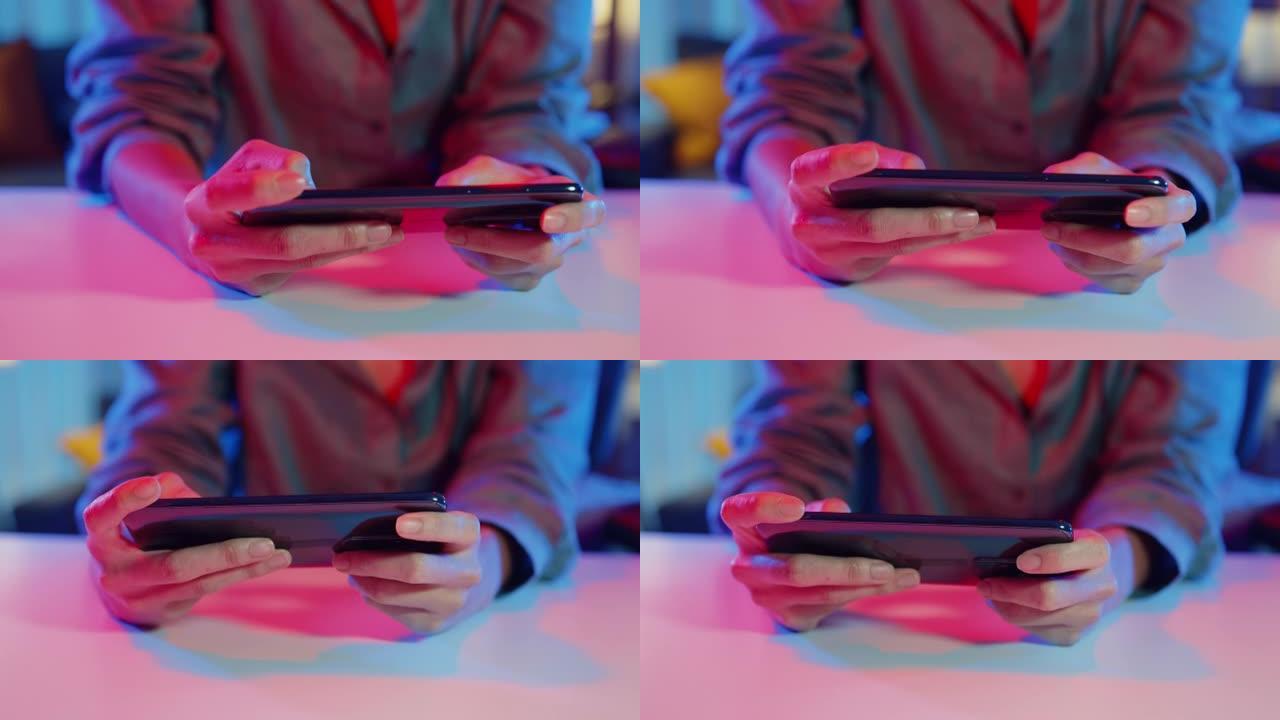 特写镜头亚洲女孩游戏玩家使用智能手机玩网络游戏彩色霓虹灯在客厅的桌子上在家。