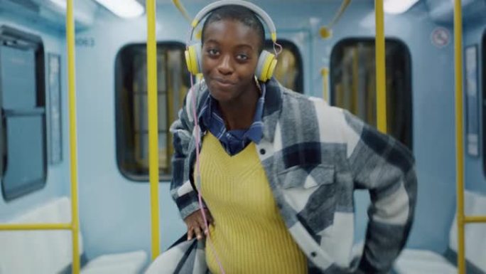 年轻时尚的黑人妇女戴上耳机，在空荡荡的电车上随着歌曲的节奏跳舞。无忧无虑的非洲裔美国少年通过快乐的音