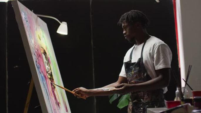 非裔美国男性艺术家在艺术工作室的画布上穿着围裙绘画