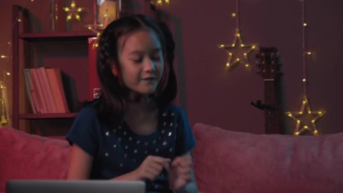 迷人的亚洲小女孩在笔记本电脑屏幕前跳舞，通过视频通话与她的朋友聚会。三个兄弟姐妹在客厅用vdo会议技