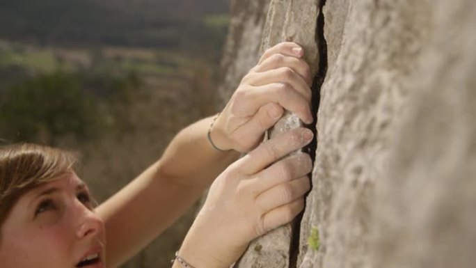 特写: 健康的女性领头登山者在巨大的悬崖上抓住了一个片状的抓地力。