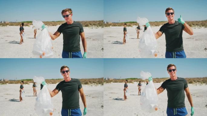 一位戴着墨镜的年轻男性志愿者的慢动作在镜头前微笑着，满足于在大海的海滩上捡起塑料垃圾以保护环境。