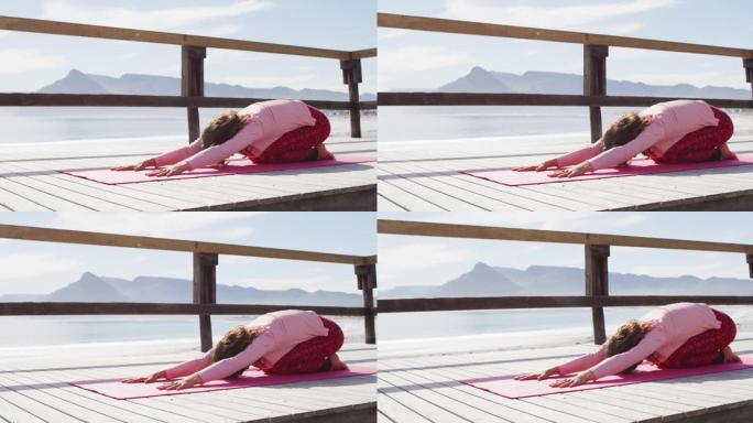 健康的混血女子在户外练习瑜伽，跪在海边伸展