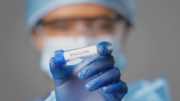 女性实验室研究人员穿着个人防护用品，手持标有疫苗的试管的特写