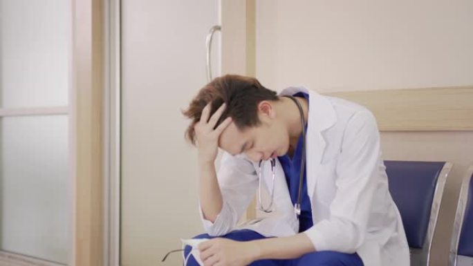 年轻的亚洲医生坐在医院走廊感觉疲倦，沮丧，悲伤，疲劳，问题，倦怠压力和不安或担心的工作。医疗职业概念