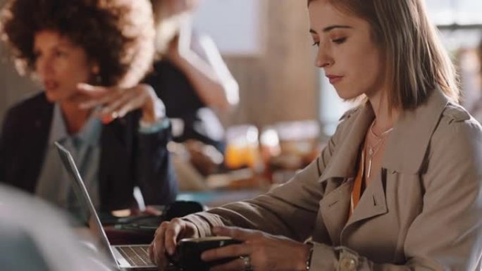 年轻女子使用笔记本电脑在咖啡馆工作，在智能手机社交媒体上输入电子邮件共享消息，享受坐在繁忙的餐厅喝咖