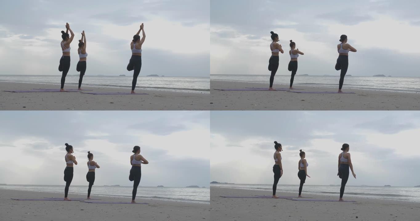 三人一组体育课，在日出的早晨在海滩上一起练习瑜伽课。健身课程概念。